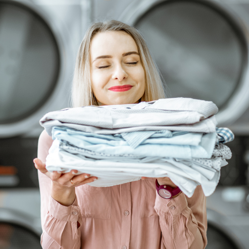Chica en la lavandería oliendo después del lavado y secado de la ropa.